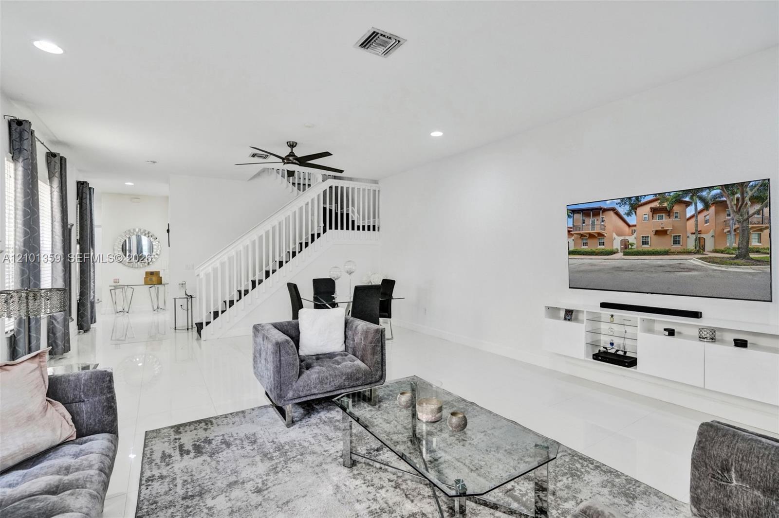 Living area featuring polished tile flooring, recessed lighting, a ceiling fan, a staircase with a white railing, and wall-mounted cabinetry
