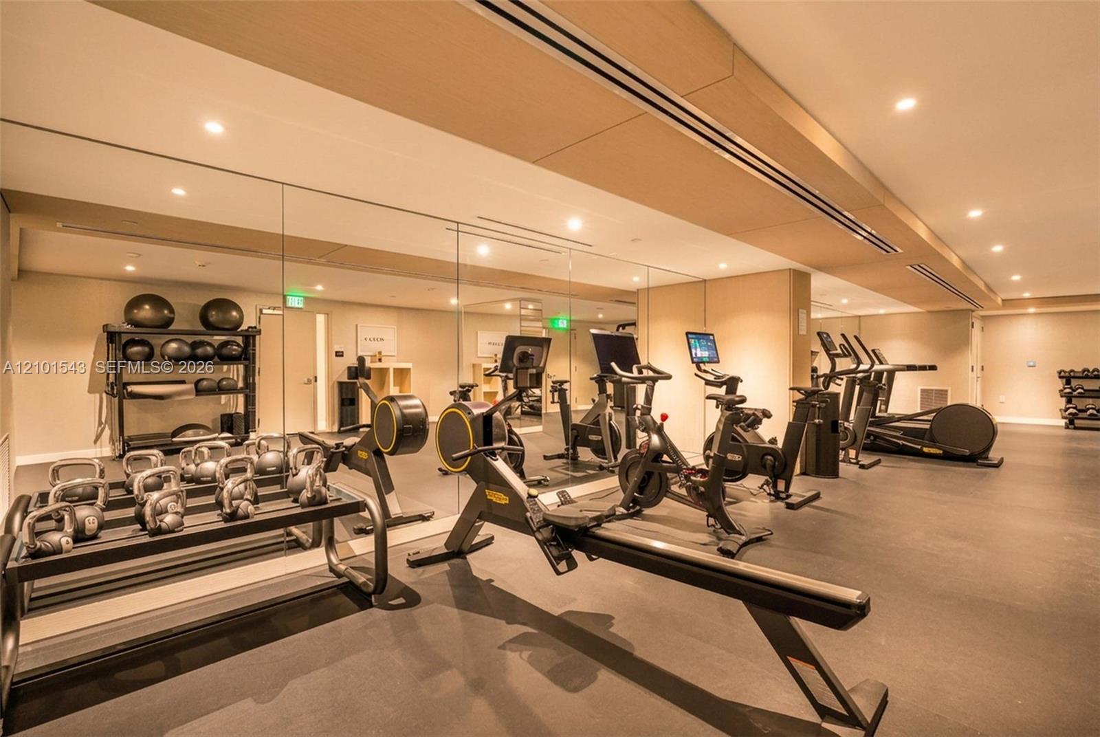 Fitness space featuring rubberized flooring, expansive floor-to-ceiling mirrored walls, recessed lighting, and wood-finish ceiling accents