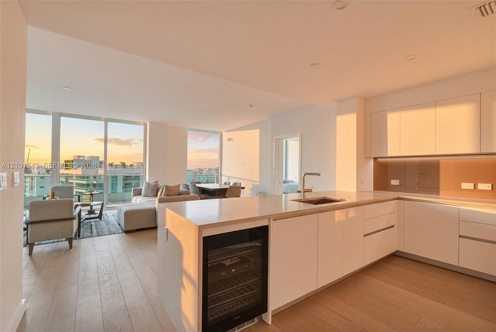 Kitchen featuring high-gloss cabinetry, stone countertops, integrated wine refrigeration, wood-finish flooring, and floor-to-ceiling windows Kitchen featuring high-gloss cabinetry, stone countertops, integrated wine refrigeration, wood-finish flooring, and floor-to-ceiling windows