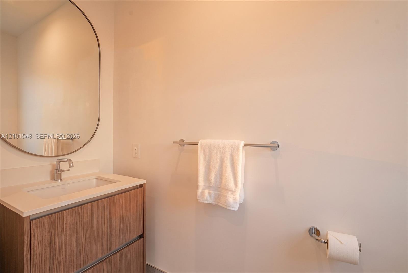 Wood-finish floating vanity with a stone-top integrated basin, polished chrome faucet, and oval wall-mounted mirror, complemented by matching chrome bathroom hardware Wood-finish floating vanity with a stone-top integrated basin, polished chrome faucet, and oval wall-mounted mirror, complemented by matching chrome bathroom hardware