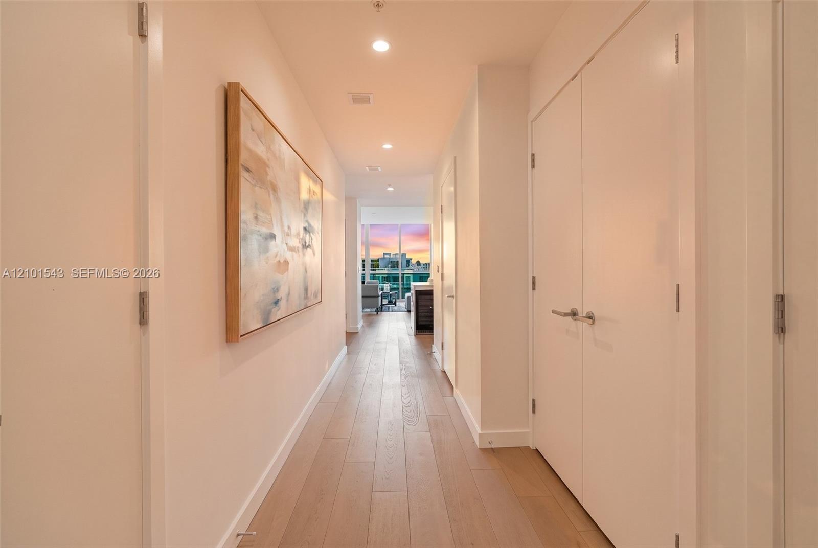 Interior hallway featuring wood-finish flooring, recessed ceiling lighting, and floor-to-ceiling double-door closets with satin-finish hardware