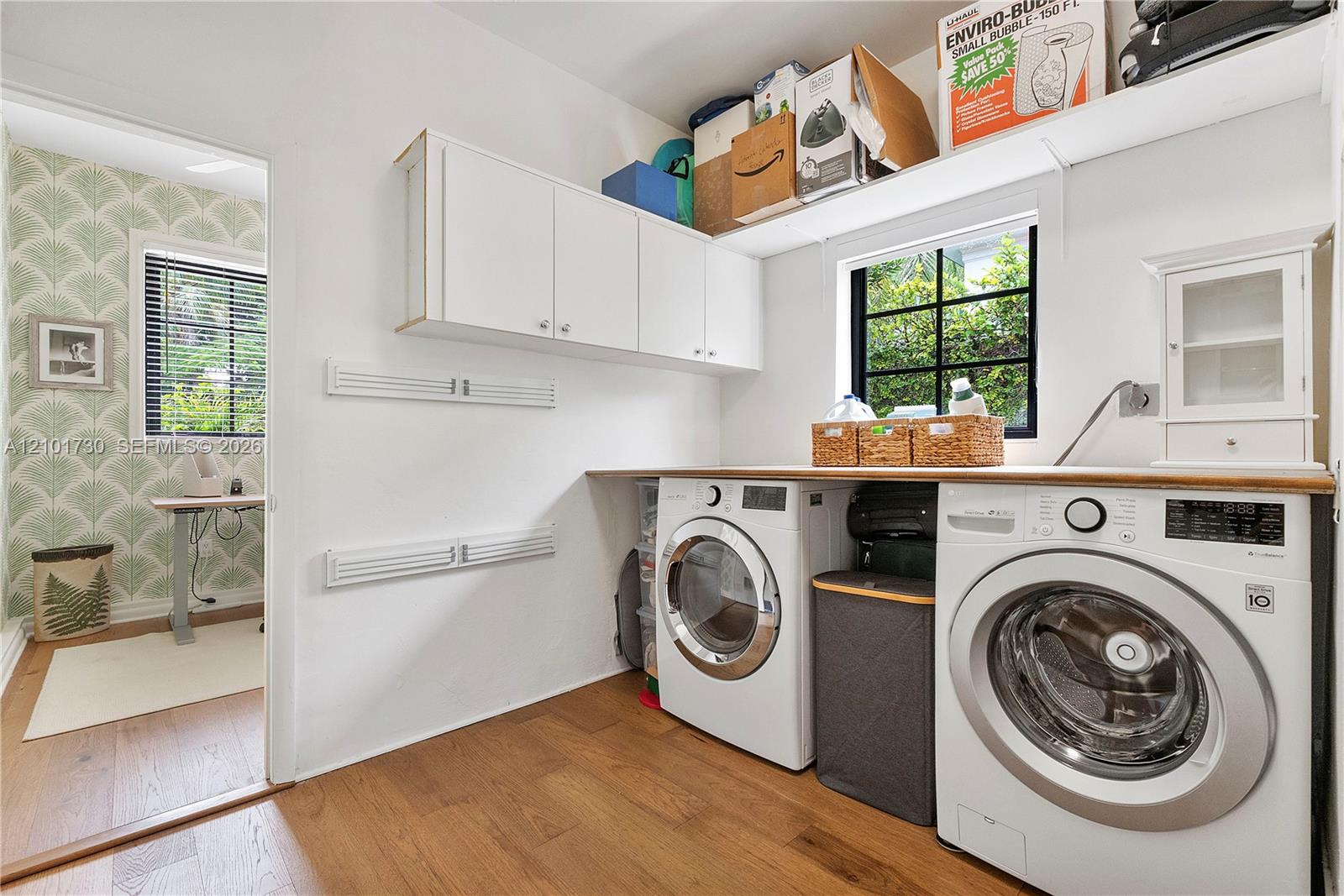 Laundry area featuring white wall-mounted cabinetry, wood-finish flooring, a wood-surface countertop, and a window with black grid mullions