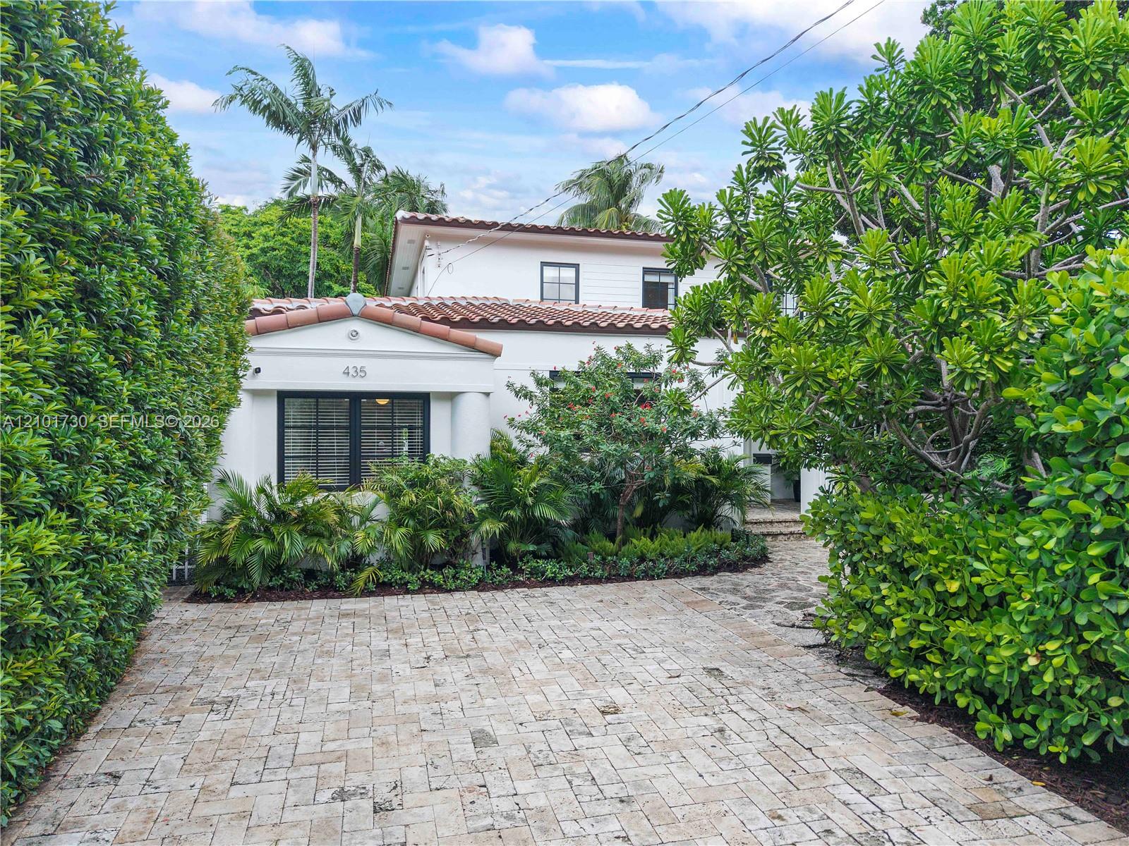 Exterior facade featuring a white stucco finish, decorative tile roof, multi-pane dark-framed windows, and a paved stone driveway
