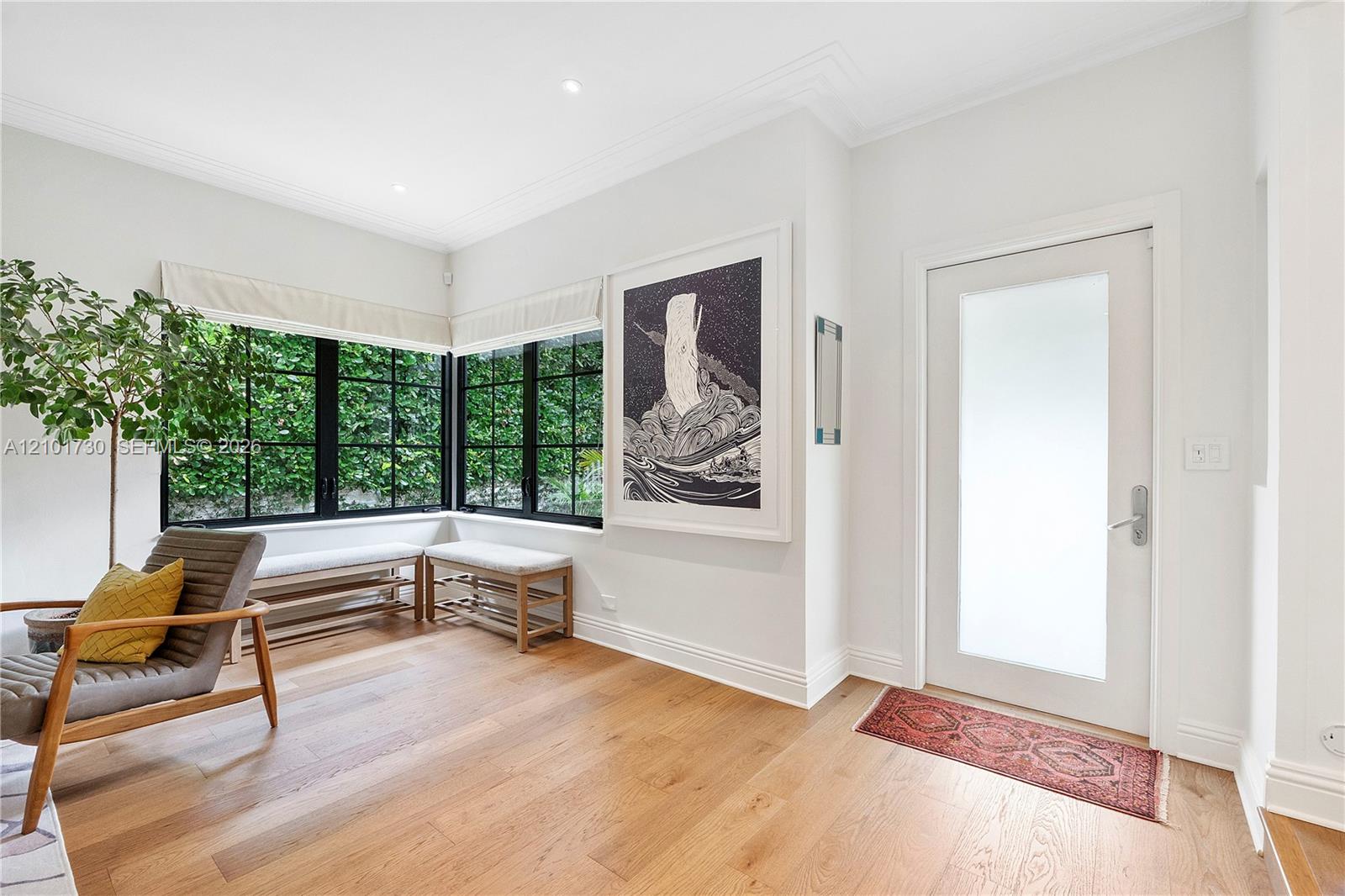 Entryway featuring wide-plank wood-finish flooring, recessed lighting, crown molding, a frosted-glass pane entry door, and floor-to-ceiling corner windows with black mullions