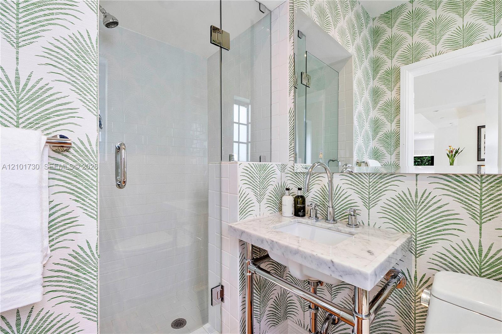 Wall-mounted washbasin with stone countertop, polished metal console legs, glass-enclosed shower featuring white subway tile, and wall-mounted faucet