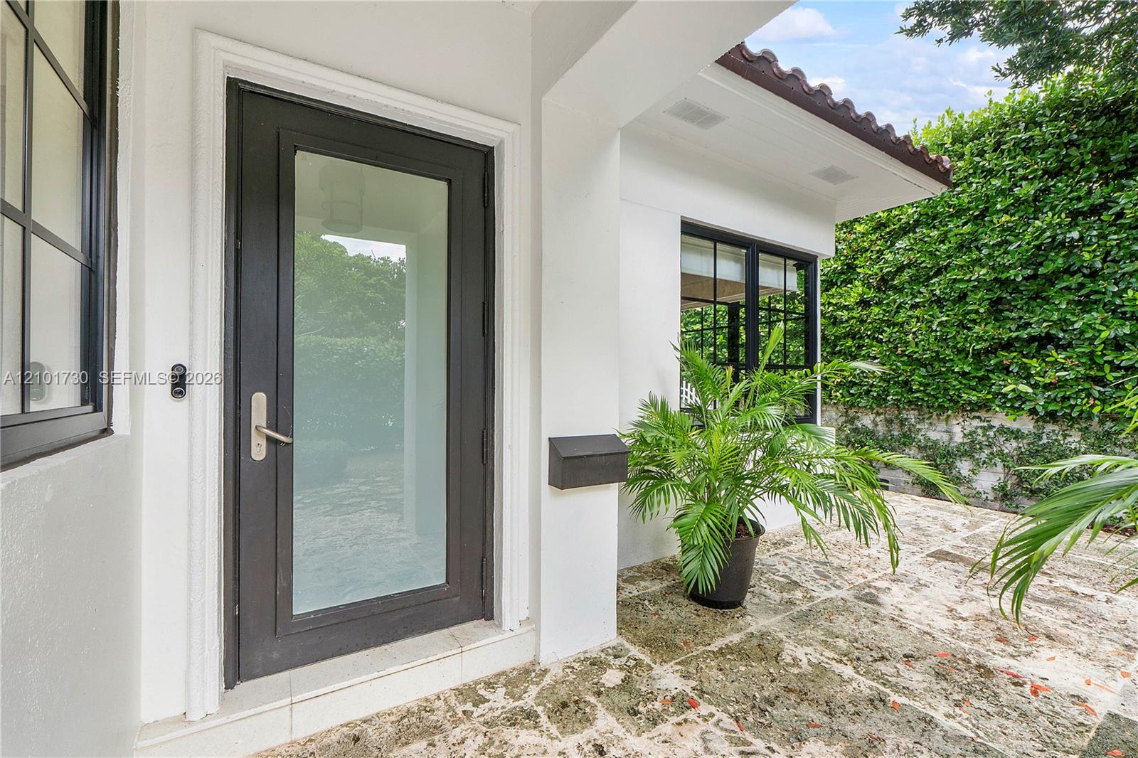 Entryway featuring a dark-framed glass door, natural stone paver flooring, a tile-accented roofline, and multi-pane windows with dark framing