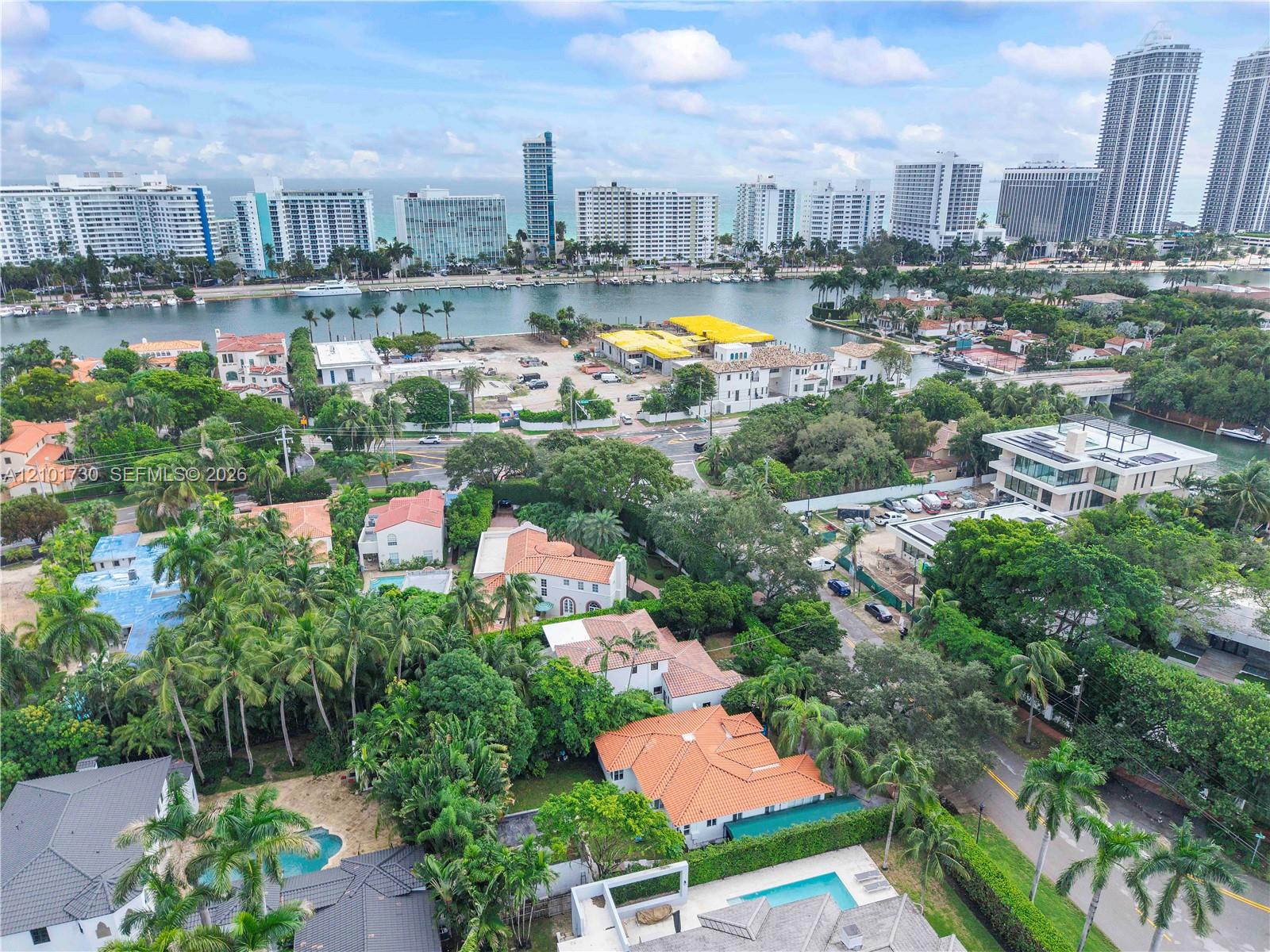Aerial perspective of a coastal residential area featuring tile roofing, mature tropical foliage, private swimming pools, and proximity to the waterfront