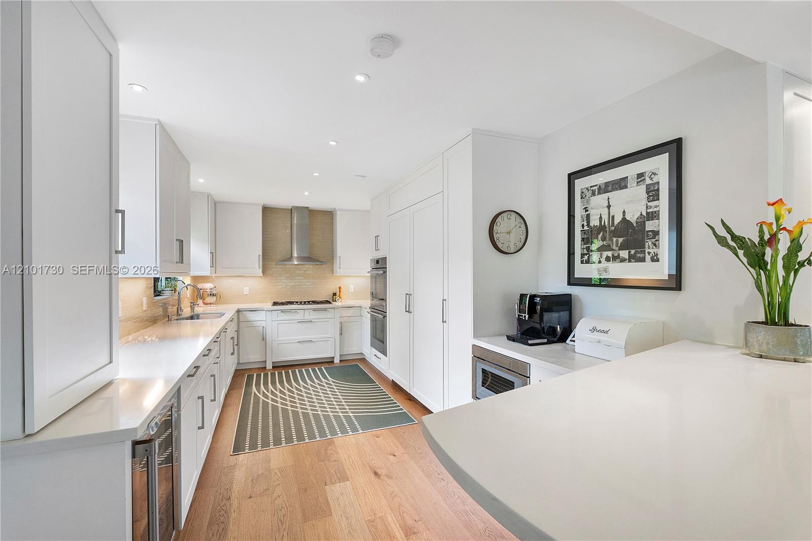 Kitchen featuring white cabinetry, solid-surface countertops, wood-finish flooring, built-in stainless steel appliances, and a tiled backsplash