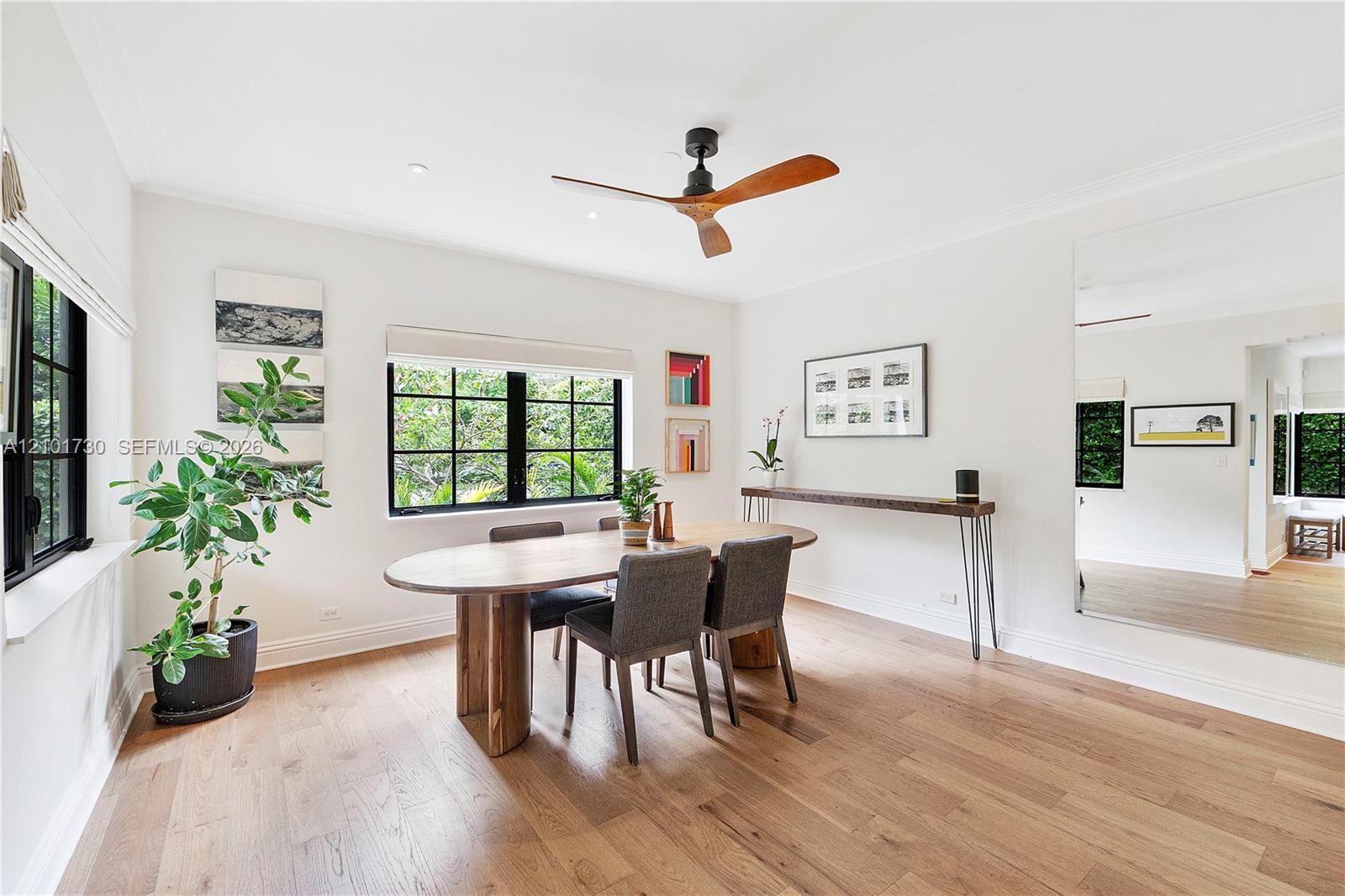 Spacious room featuring wood-finish flooring, black-framed windows, a ceiling fan with wood-tone blades, and a large wall-mounted mirror