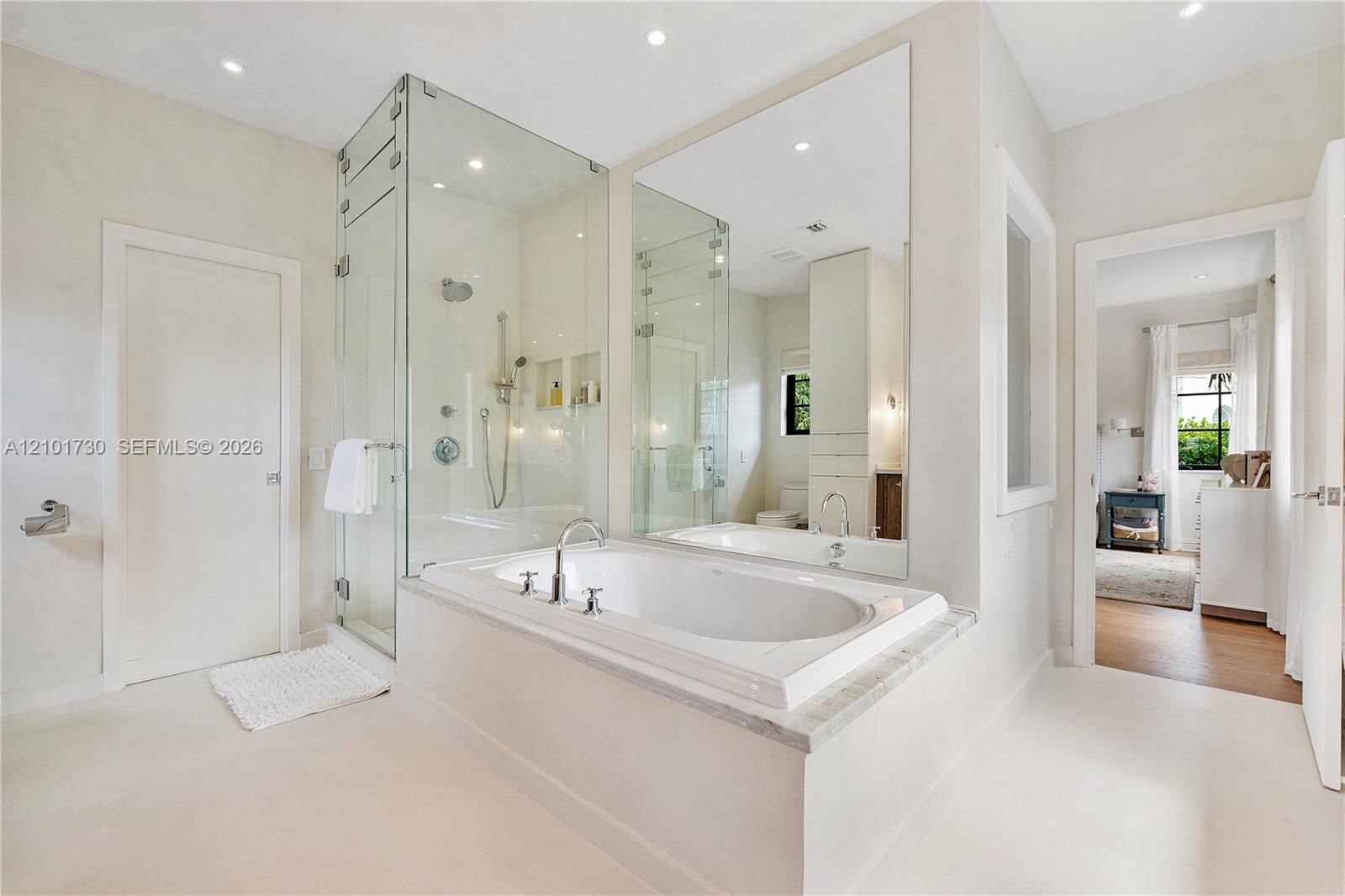 Soaking tub with a stone-surround deck, glass-enclosed walk-in shower, wall-to-wall mirror, and recessed lighting