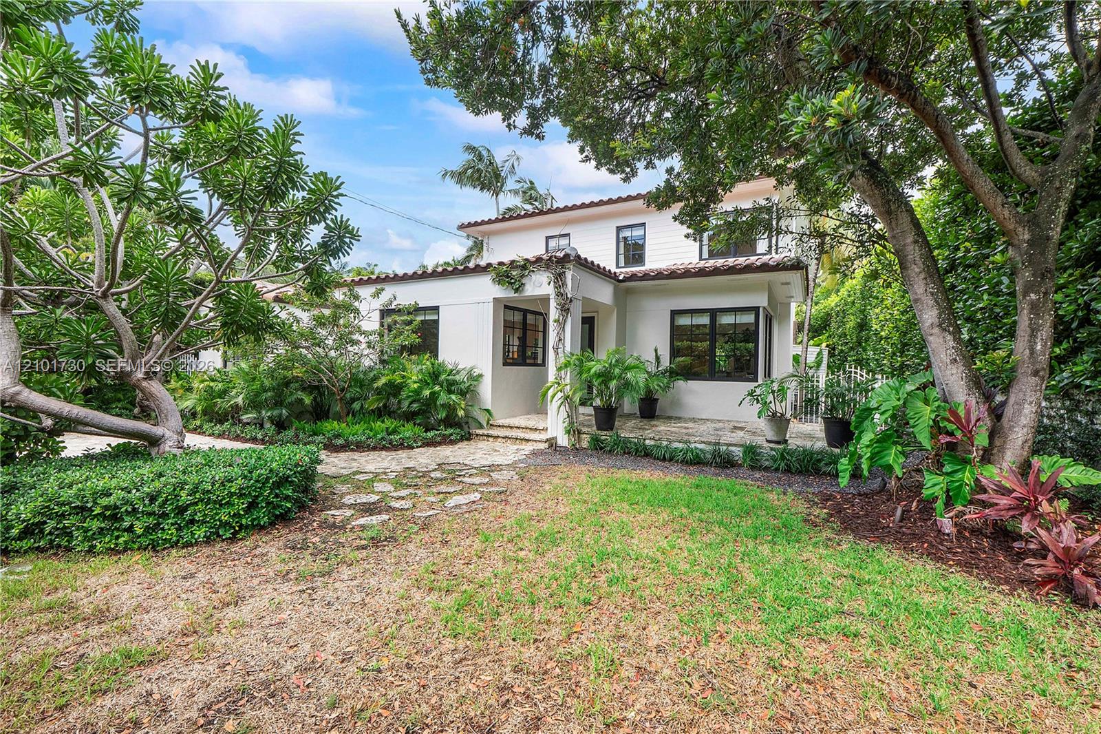 Two-story residence featuring a smooth stucco exterior, multi-pane windows, a tile roof, and a natural stone-paved patio surrounded by mature landscape