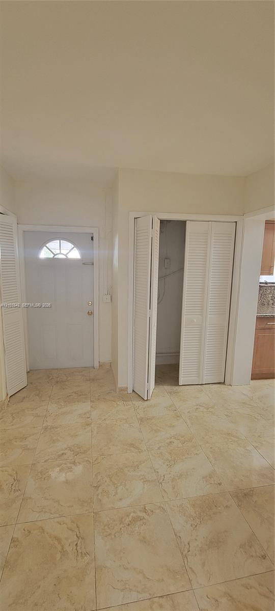 Entryway featuring light-toned tile flooring, a white paneled door with a semi-circular transom window, and dual white louvered closet doors