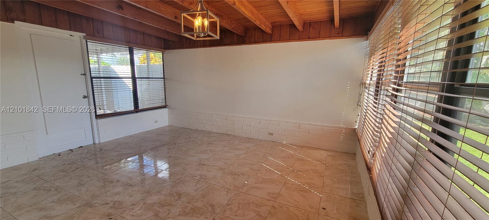 Sunroom featuring a vaulted wood-beam ceiling, large-format tile flooring, exposed painted brick wainscoting, and large windows with horizontal blinds