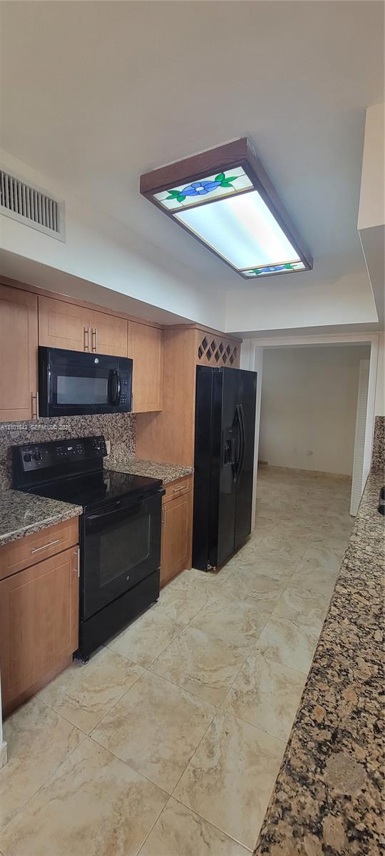 Kitchen featuring wood cabinetry with built-in wine storage, stone countertops, black appliance suite, and stained glass flush-mount ceiling light