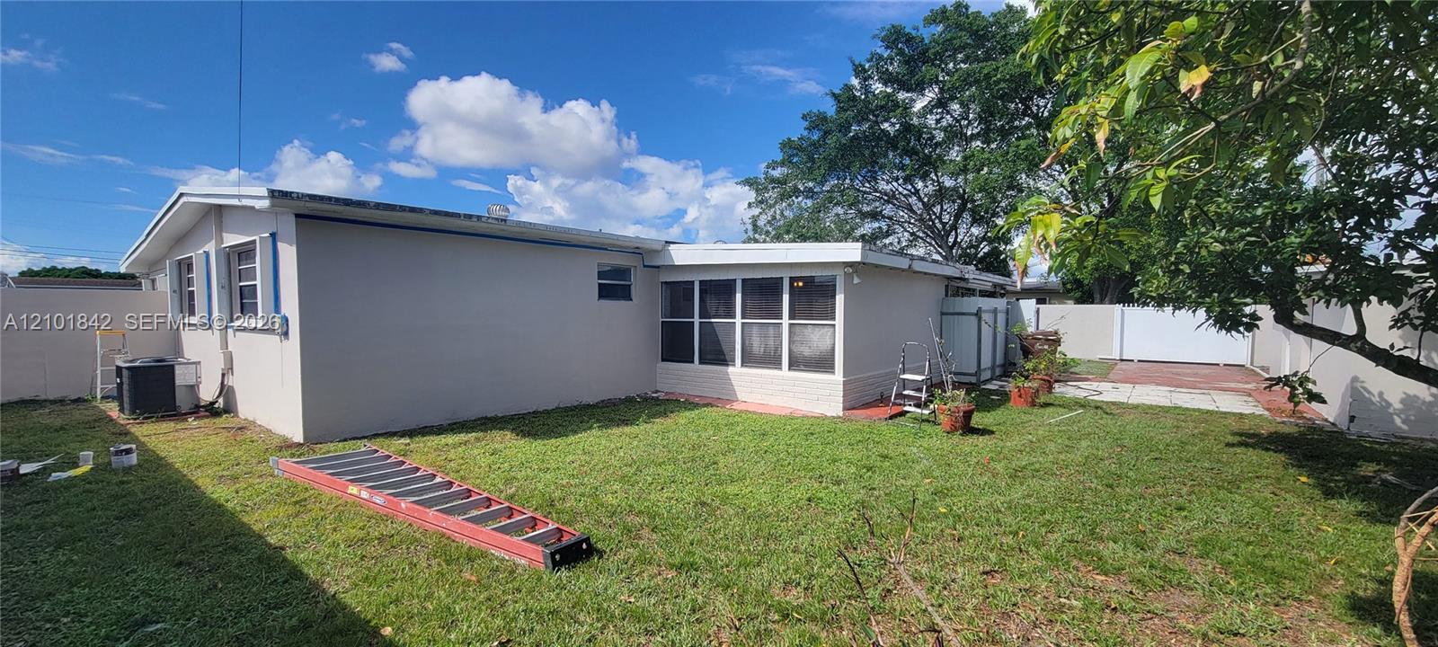 Exterior grounds featuring a grass lawn, enclosed sunroom with multi-pane windows, privacy fencing, and a concrete patio area