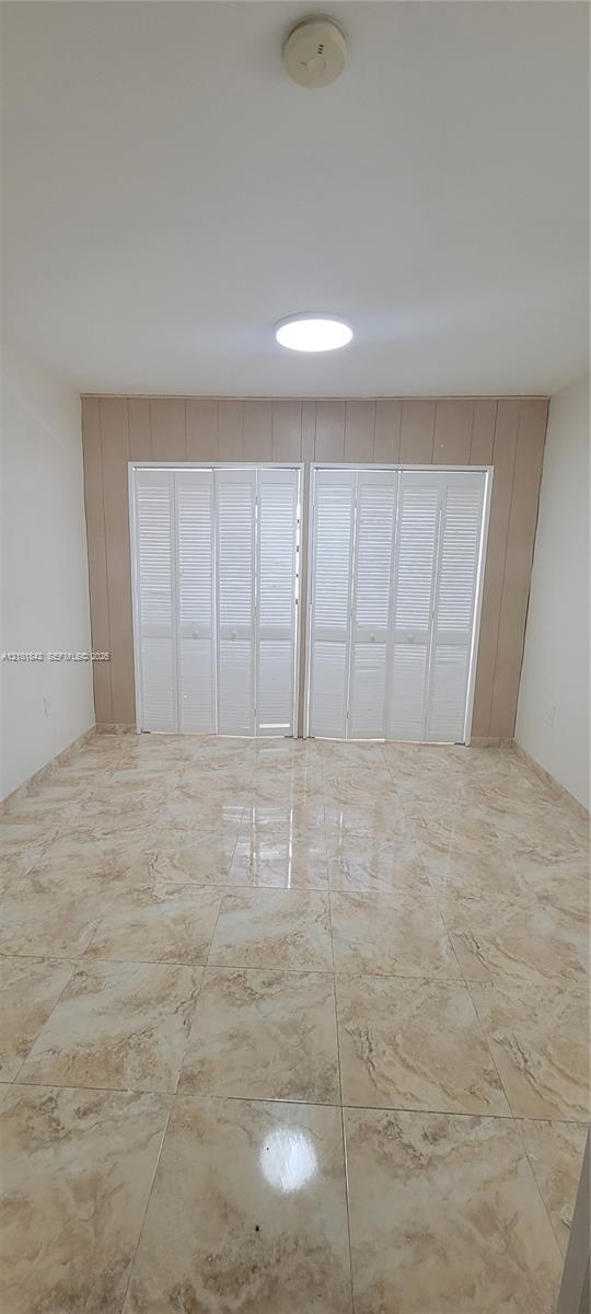Large-format tile flooring, dual white louvered bifold closet doors, and recessed ceiling lighting