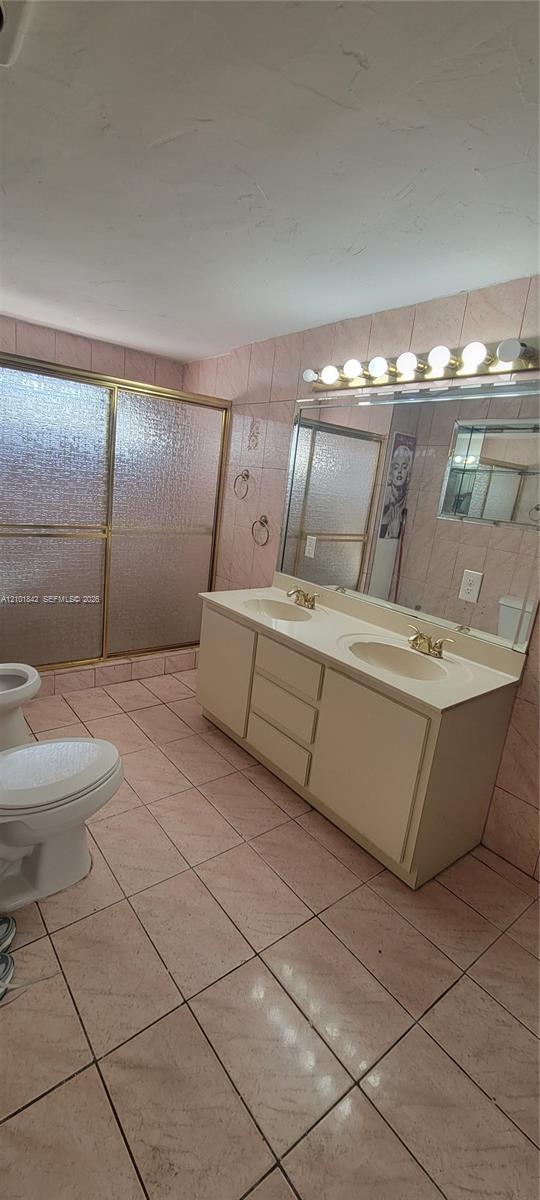 Double vanity with integrated sinks, large wall-mounted mirror, brass-finish fixtures, and walk-in shower with textured glass enclosure