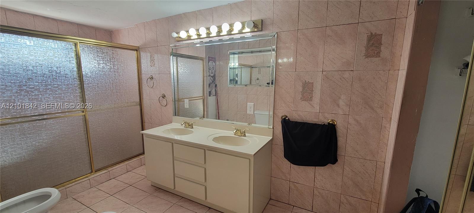 Dual-sink vanity with a solid-surface countertop, full-width vanity mirror, eight-bulb horizontal light fixture, and floor-to-ceiling ceramic tile wall detailing