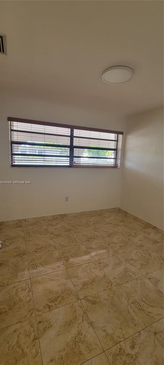 Neutral-toned tile flooring, horizontal window blinds, and a flush-mount circular ceiling fixture