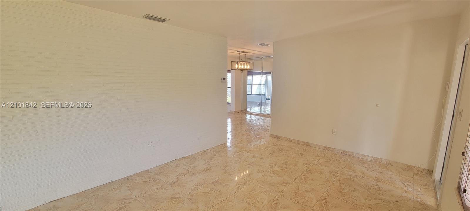 Interior space featuring white-painted brick walls, polished tile flooring, and a multi-light metal chandelier