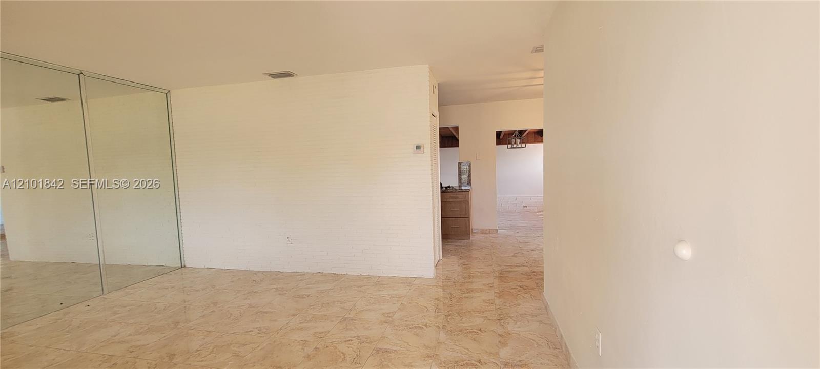 Interior space featuring large-format polished tile flooring, floor-to-ceiling mirrored wall paneling, and painted brick wall surfacing