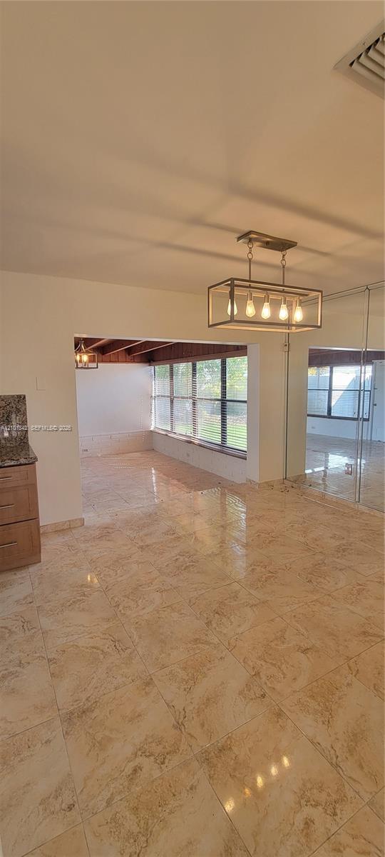 Polished stone-finish tile flooring, rectangular geometric chandelier with five exposed bulbs, mirrored wall paneling, and large-paned windows featuring exposed wood-beam ceiling detailing