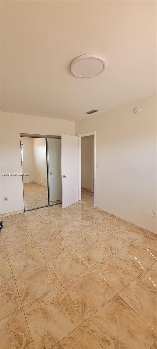 Room featuring polished stone-finish floor tiling, a sliding dual-panel mirrored closet, and a flush-mount circular ceiling fixture