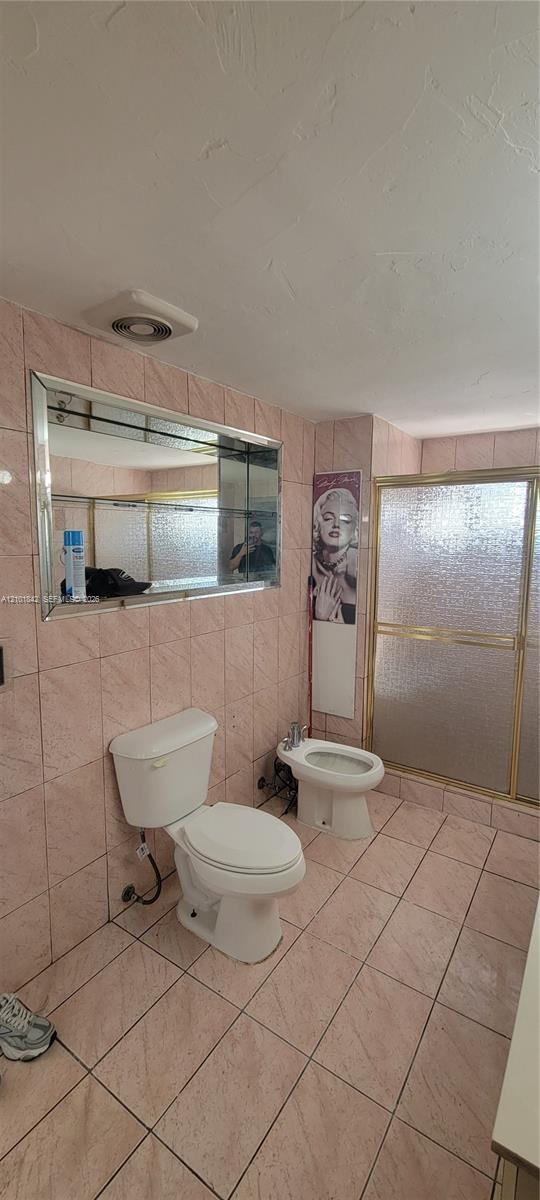 Bathroom featuring ceramic wall and floor tiling, a bidet, a glass-enclosed shower, and a built-in wall mirror