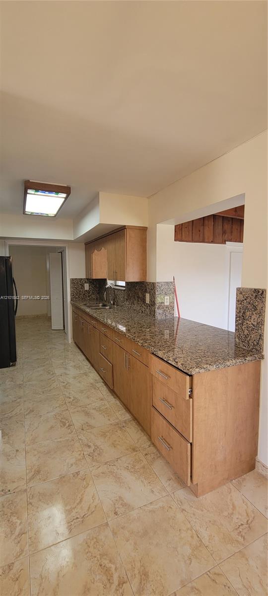 Kitchen featuring natural wood-finish cabinetry, stone countertops, stone tile flooring, and rectangular flush-mount ceiling lighting