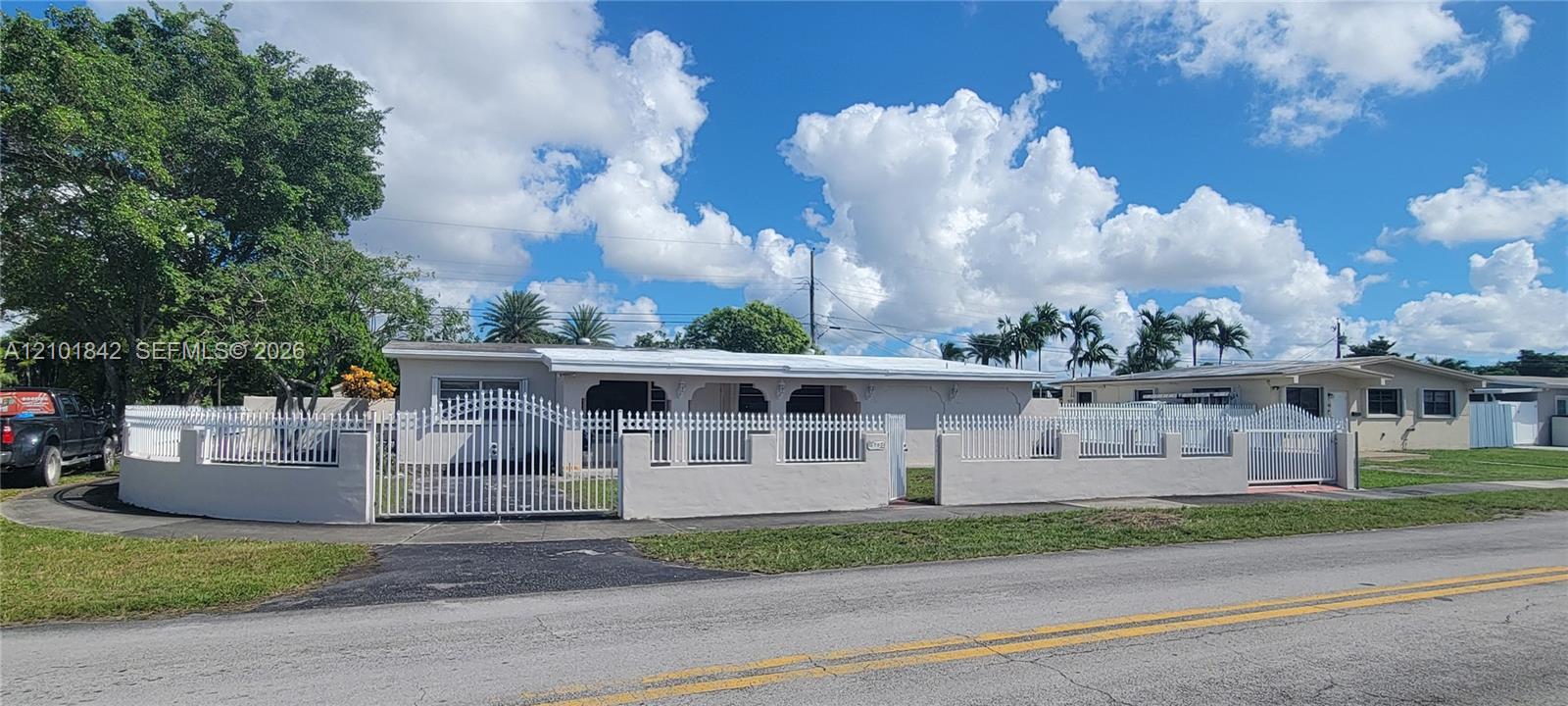 Single-story residence featuring a gated perimeter wall, white metal fencing, a covered front entryway, and an expansive lawn