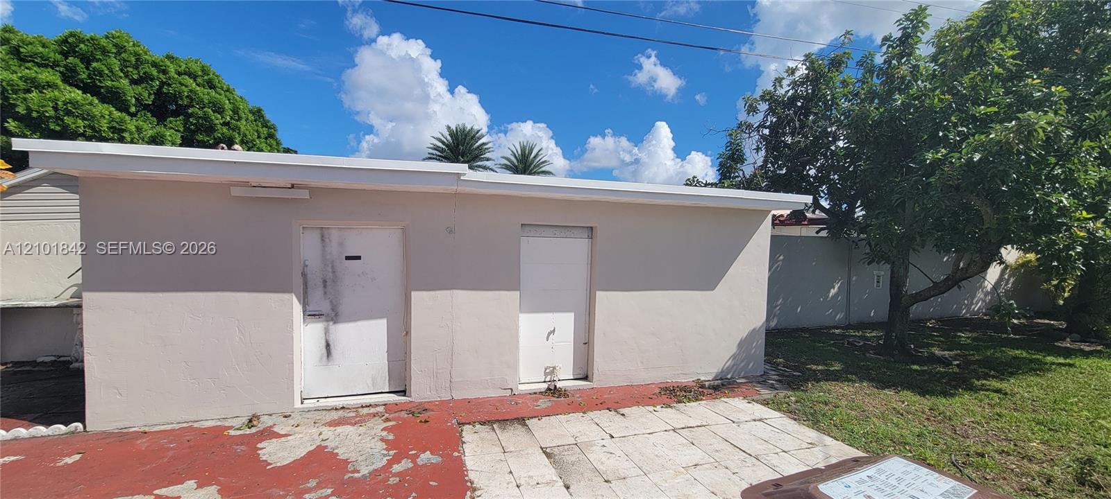 Detached exterior structure with smooth stucco siding, flat roofline, two solid-core doors, and paved patio area