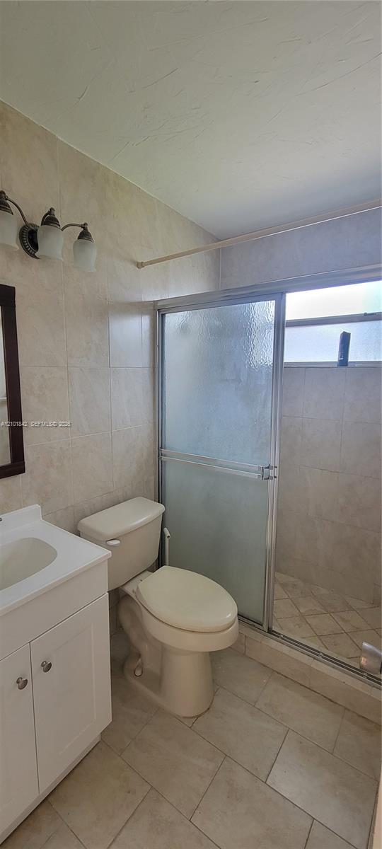 Bathroom featuring tile flooring, full-height wall tile surrounding the shower enclosure, a white vanity with an integrated sink, and a multi-light wall-mounted fixture