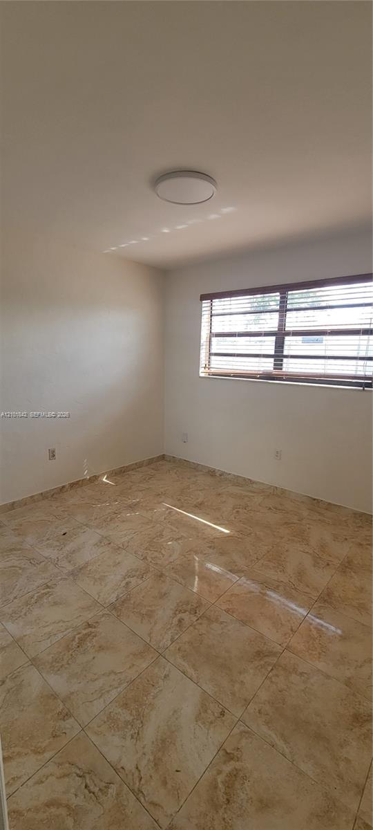 Neutral-toned ceramic tile flooring, solid-surface wall finishes, ceiling-mounted light fixture, and window with horizontal blinds