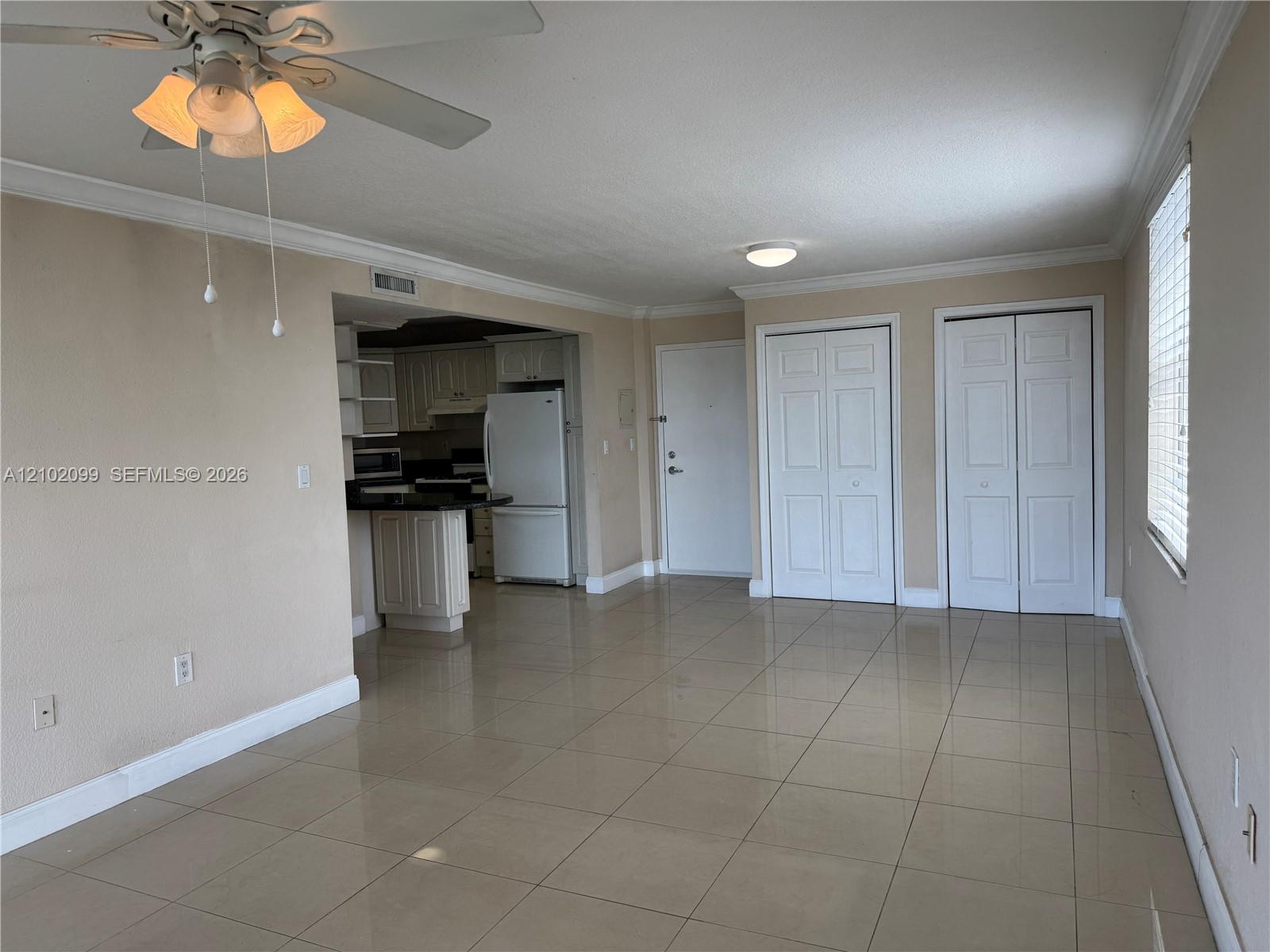 Living area featuring large-format tile flooring, crown molding, double-panel closet doors, and a ceiling fan with integrated light fixture