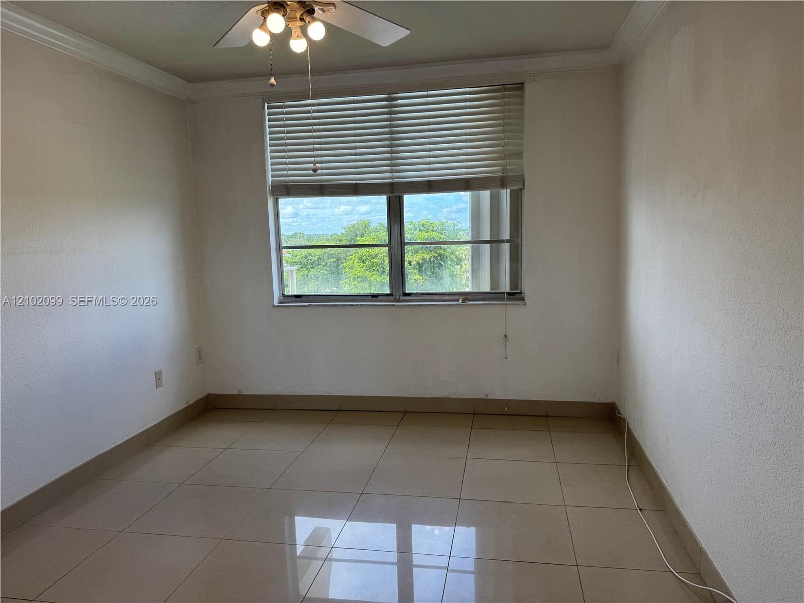 Large-format tile flooring, crown molding, expansive window with horizontal blinds, and ceiling fan with integrated lighting