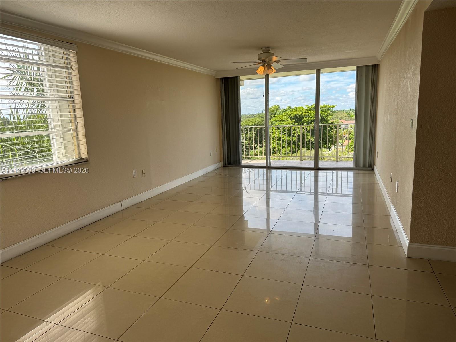 Neutral tile flooring, ceiling fan with integrated lighting, oversized sliding glass door, and a private railed balcony