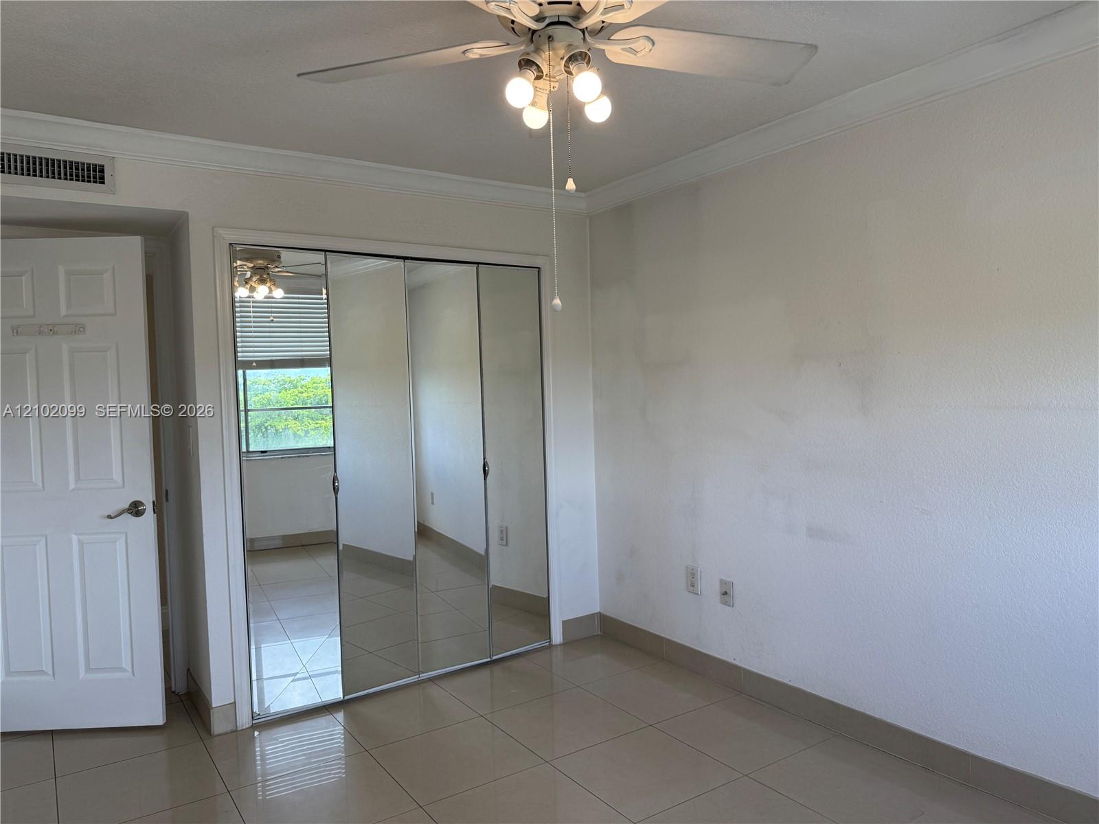 Room featuring mirrored sliding-door closet, neutral tile flooring, multi-panel interior door, and overhead ceiling fan with light fixture