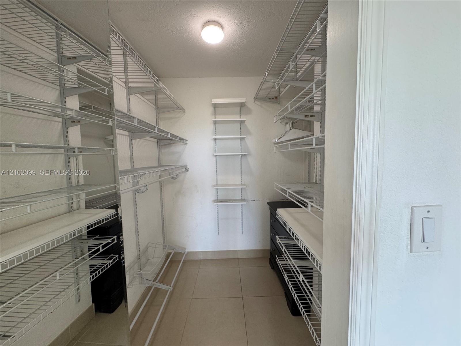 Walk-in closet featuring white wire shelving, wall-mounted racks, tile flooring, and a flush-mount light fixture