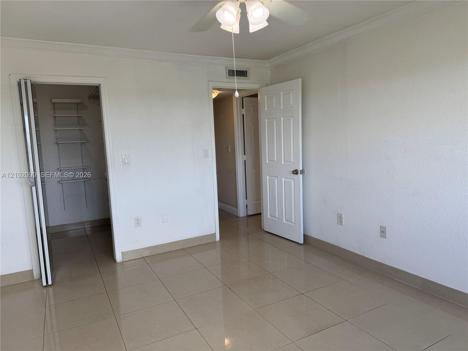 Large-format tile flooring, ceiling fan with integrated lighting, and walk-in closet with built-in shelving