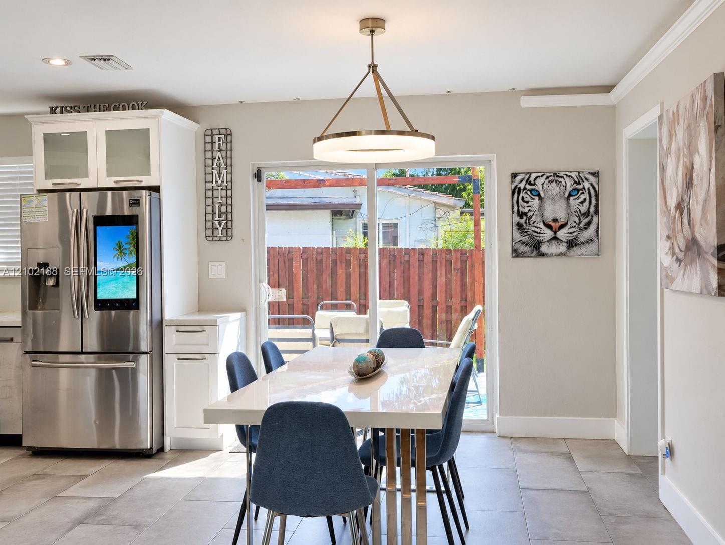 Modern kitchen featuring stainless steel refrigerator, white cabinetry with glass-panel upper doors, large-format tile flooring, and circular LED pendant lighting