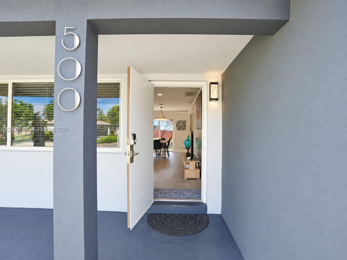 Covered entryway featuring a solid-color stucco exterior, mounted address numerals, and a sleek modern exterior sconce