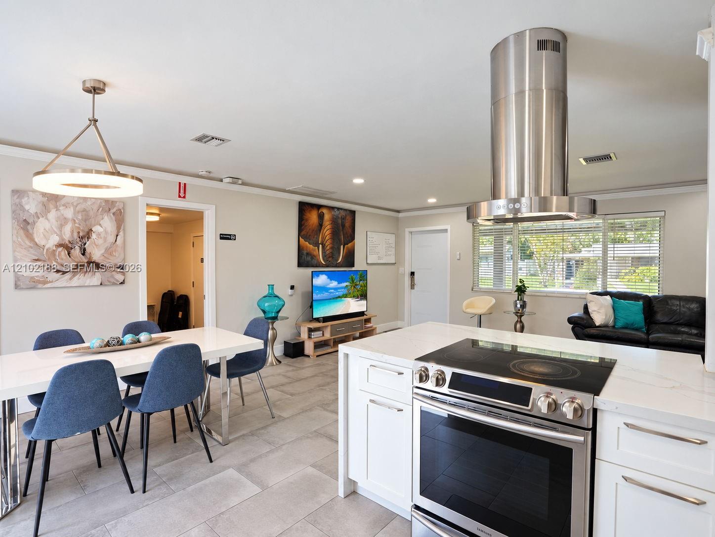 Kitchen featuring white cabinetry, quartz countertops, a stainless steel cylindrical range hood, and a built-in electric cooktop, complemented by neutral tile flooring throughout the area