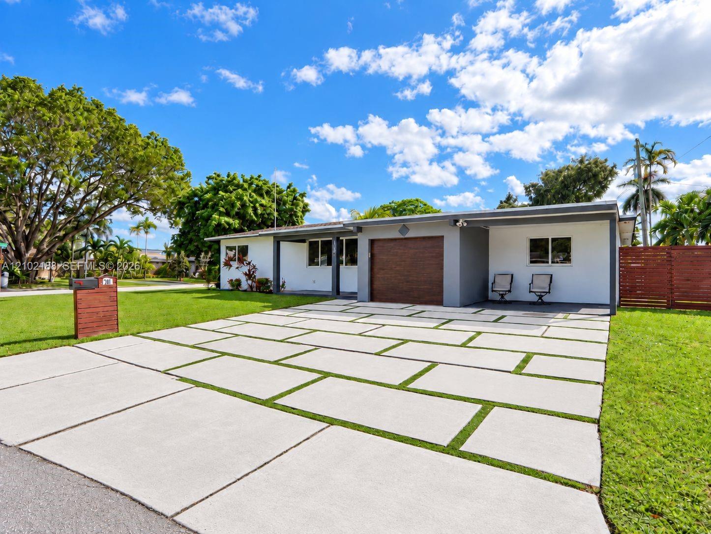 Single-story residence featuring a large-format concrete paver driveway with integrated grass joints, a wood-finish garage door, and a private side-yard wood-slat privacy fence