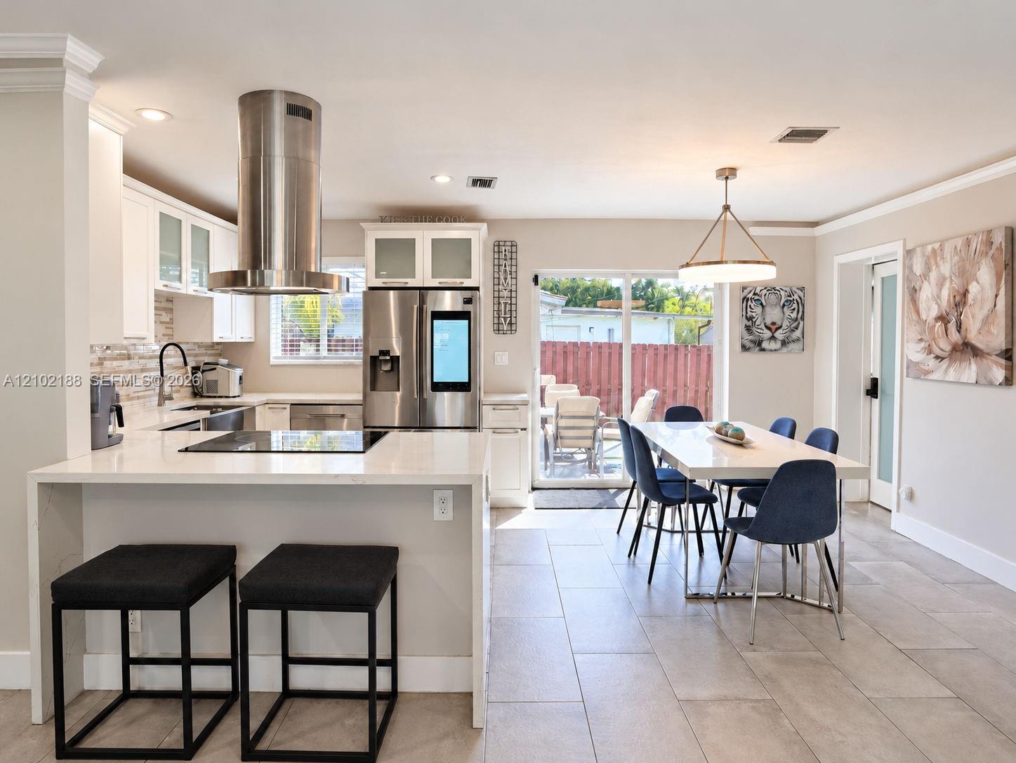 Kitchen featuring white cabinetry with glass-front uppers, stainless steel appliances including a cylinder range hood, quartz countertops, and large-format tile flooring