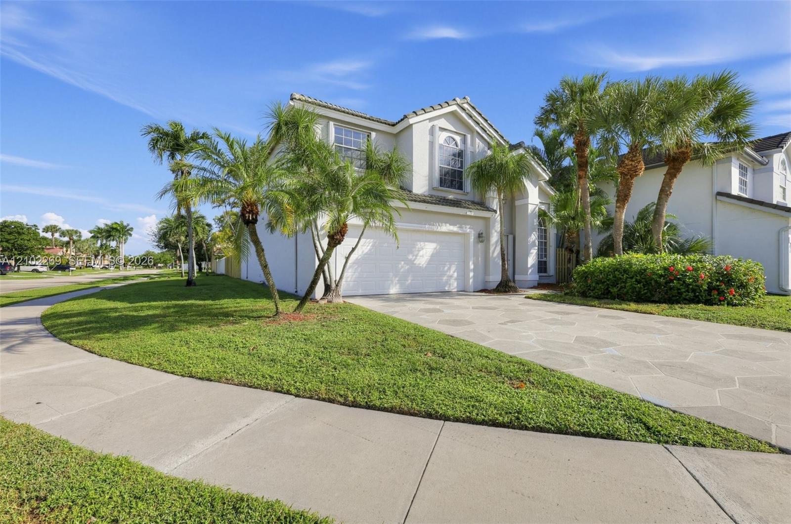 Two-story stucco exterior featuring a multi-gabled roofline, expansive concrete paver driveway, attached two-car garage, and mature palm landscaping Two-story stucco exterior featuring a multi-gabled roofline, expansive concrete paver driveway, attached two-car garage, and mature palm landscaping