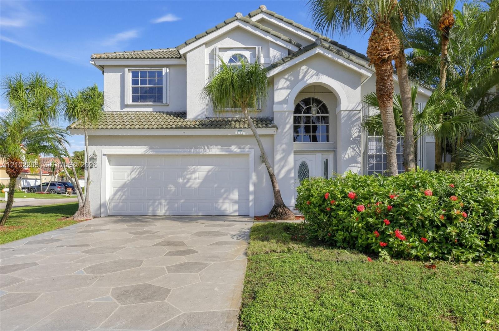 Two-story stucco exterior featuring a concrete tile roof, arched entryway with decorative glass door, multi-paned windows, and a geometric-patterned concrete driveway Two-story stucco exterior featuring a concrete tile roof, arched entryway with decorative glass door, multi-paned windows, and a geometric-patterned concrete driveway