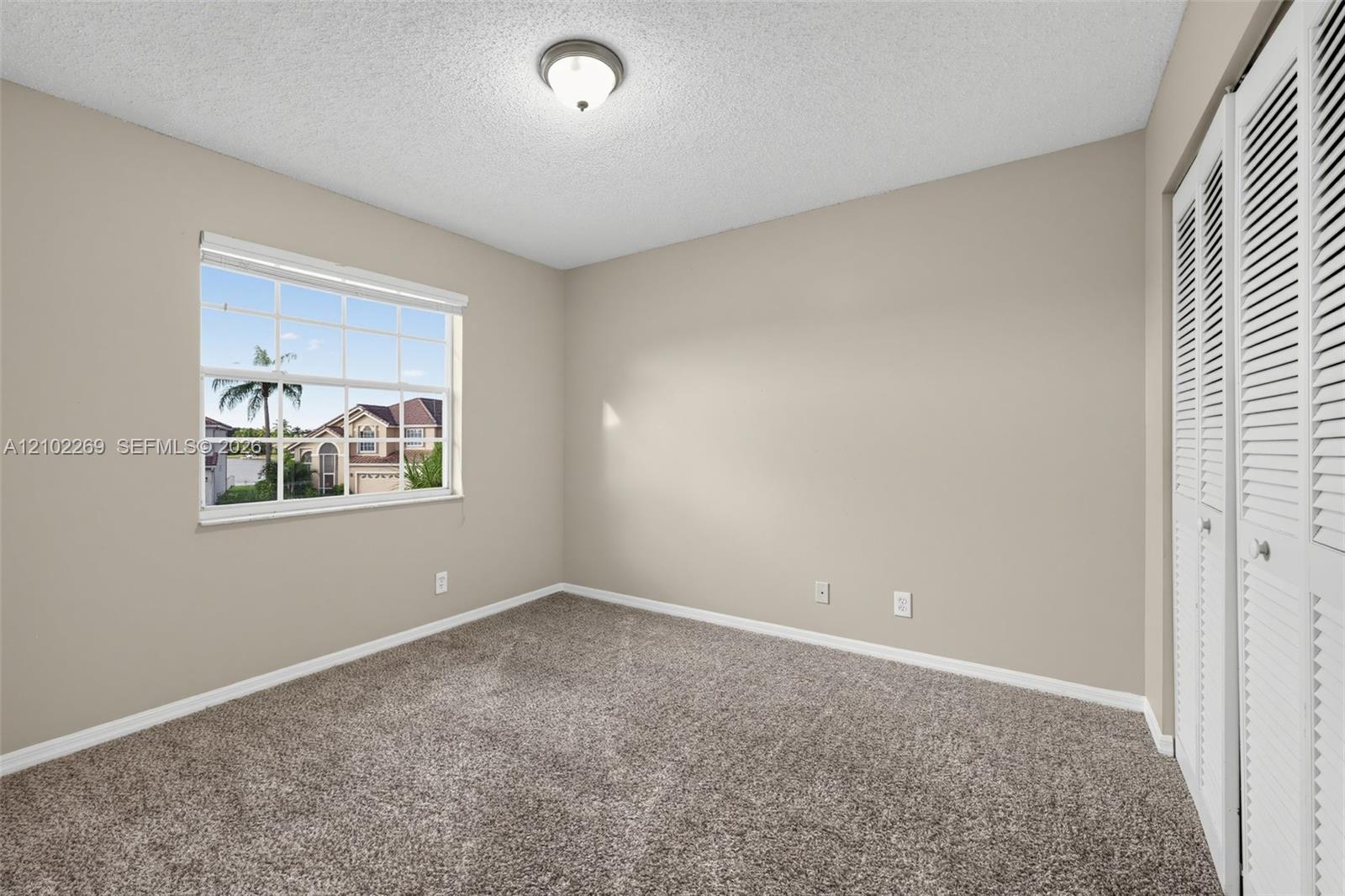 Room featuring neutral wall tones, wall-to-wall carpeting, a multi-pane window, and louvered bi-fold closet doors