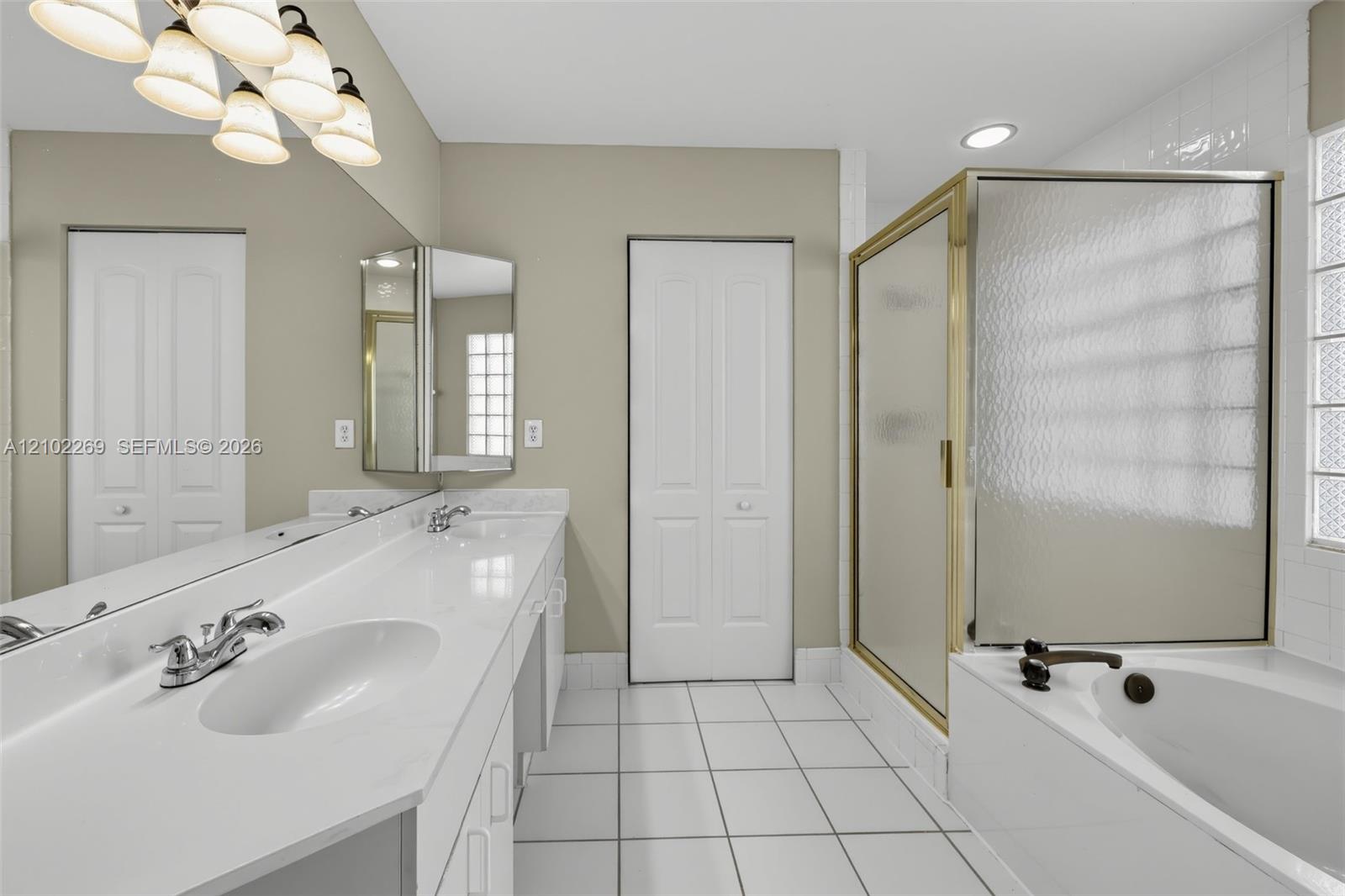 Double vanity with white solid surface countertop, glass-enclosed shower, soaking tub, and glass block window detailing