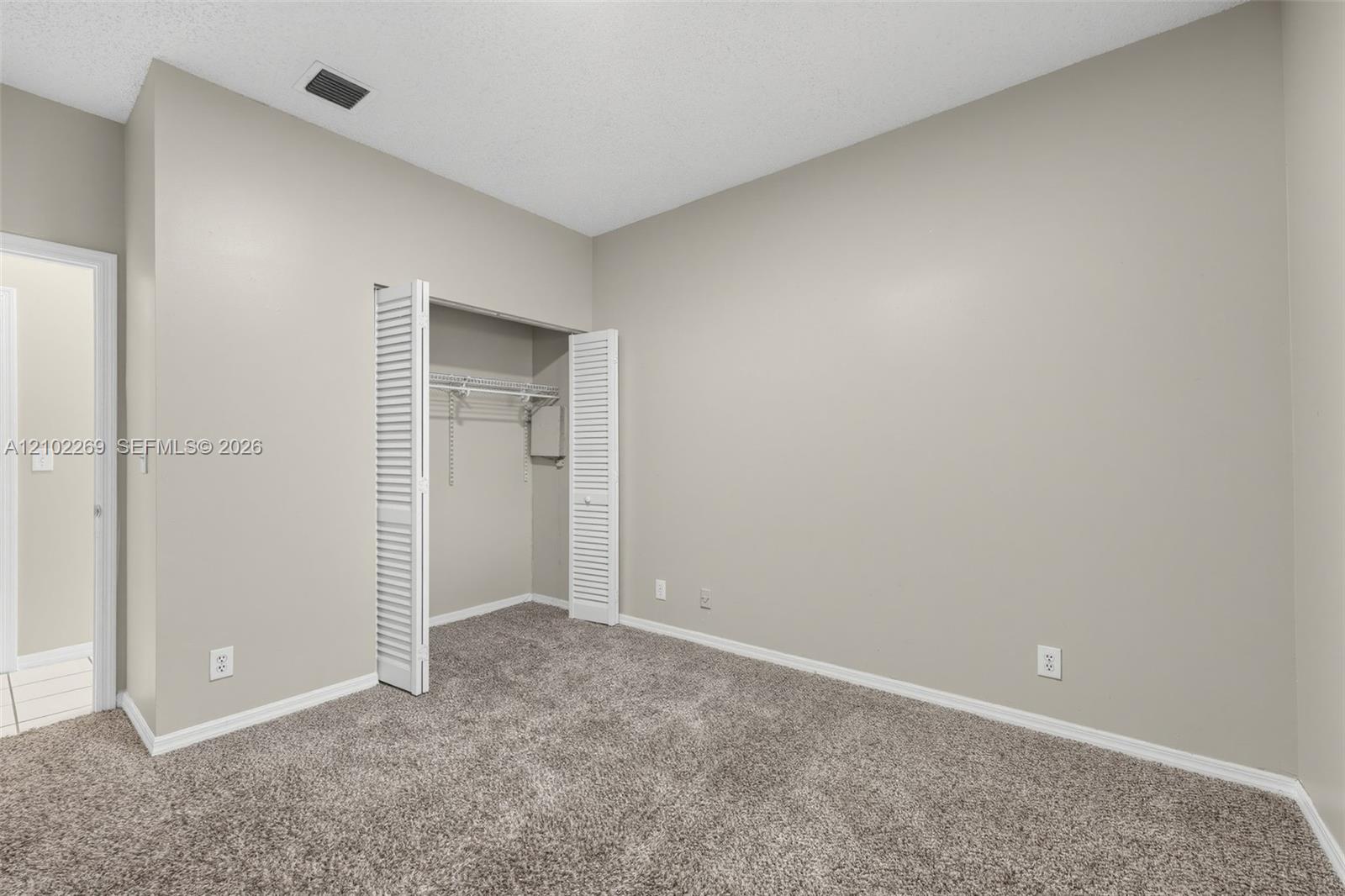 Neutral-toned interior space featuring neutral carpeting, a built-in closet with bi-fold louvered doors, and wire shelving