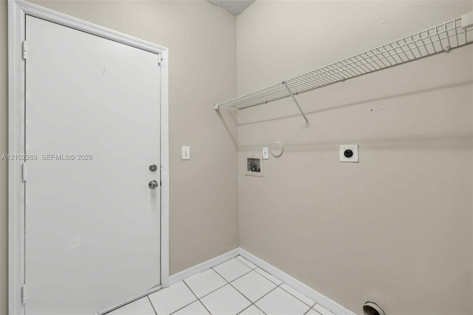 Utility area featuring white ceramic tile flooring, a solid core door, and wall-mounted wire shelving
